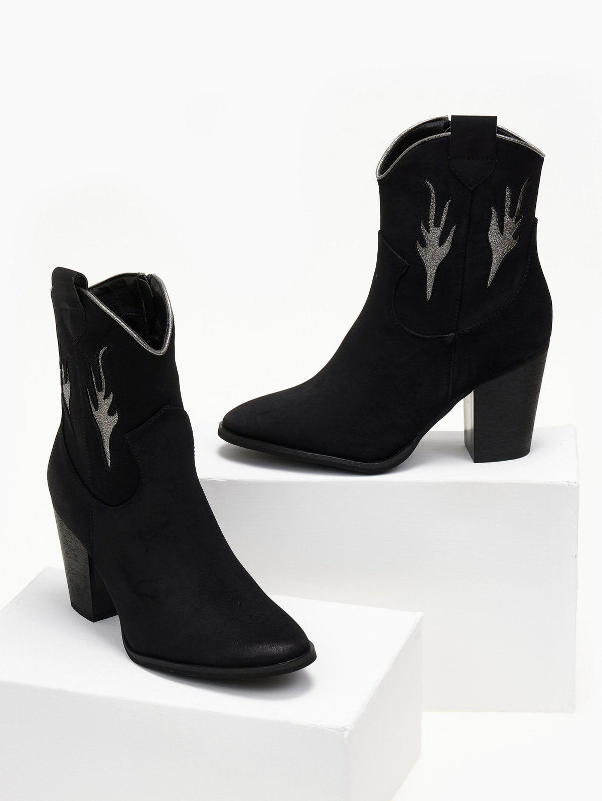 Pair of black suede cowboy ankle boots with silver flame details and block heel, displayed on white blocks