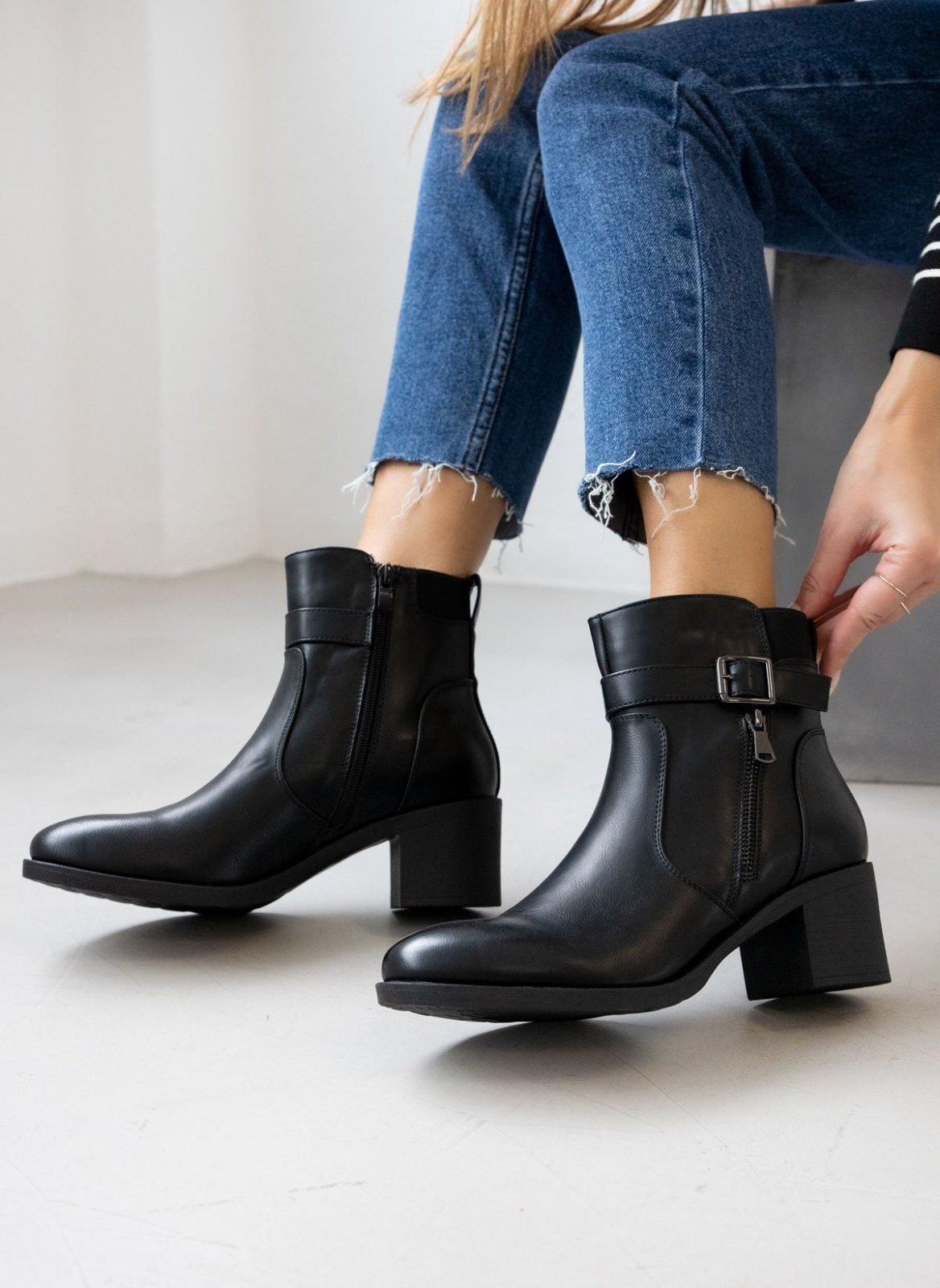 Block heel ankle boots with buckle strap and outer zipper in black faux leather, front view worn on model