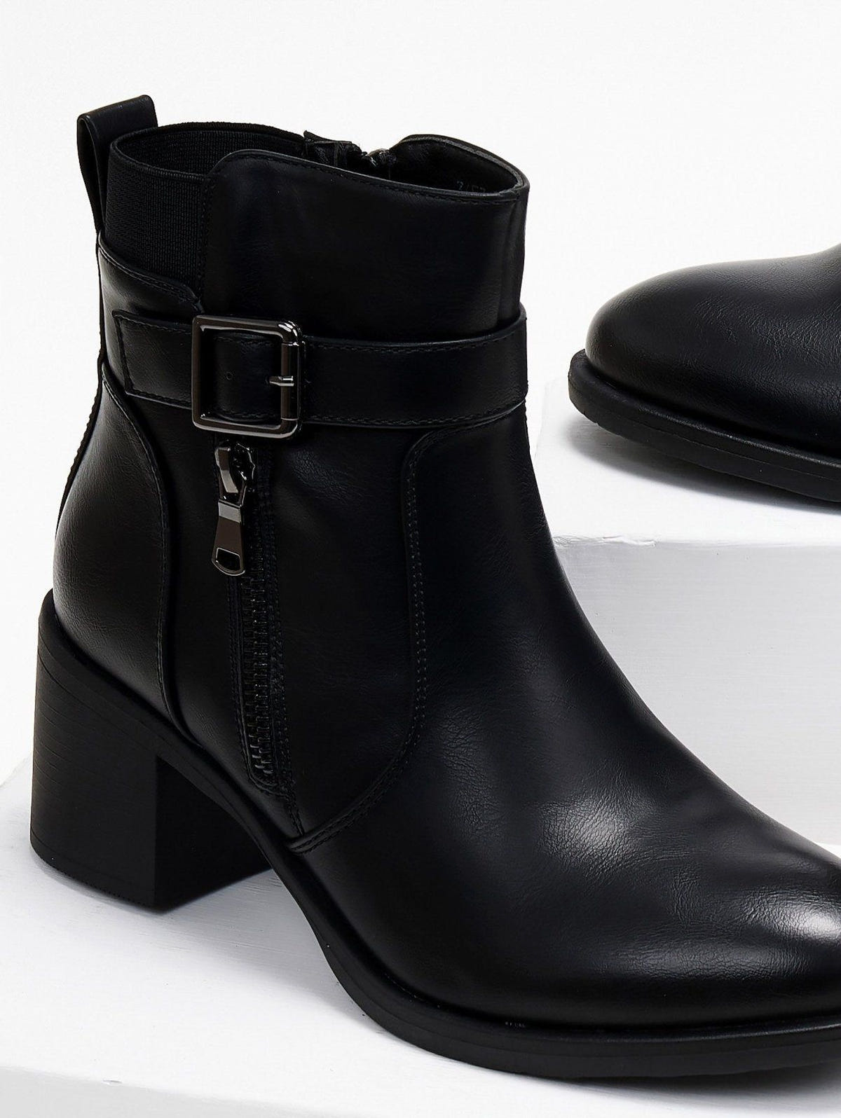 Block heel ankle boots with buckle strap and outer zipper in black faux leather, close-up of the buckle detail