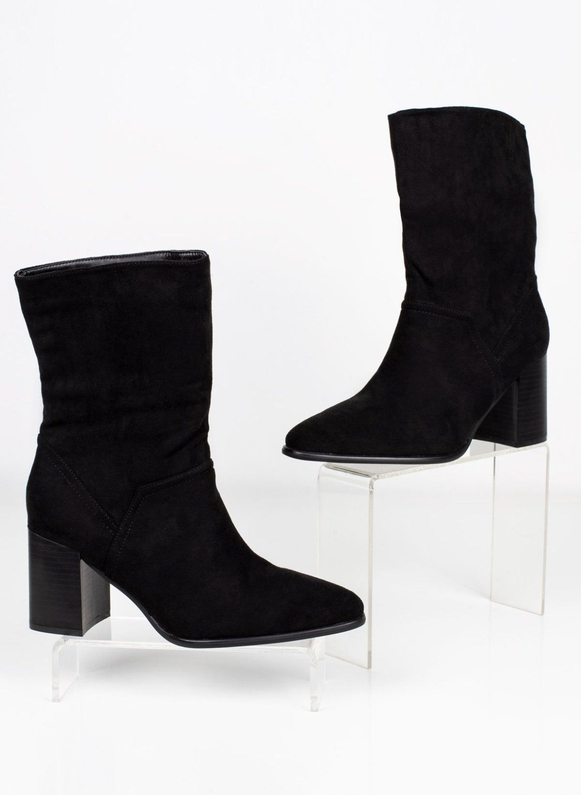 Pair of black suede block heel ankle boots with pointed toe displayed on clear stands, angled view