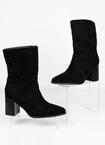 Pair of black suede block heel ankle boots with pointed toe displayed on clear stands, angled view