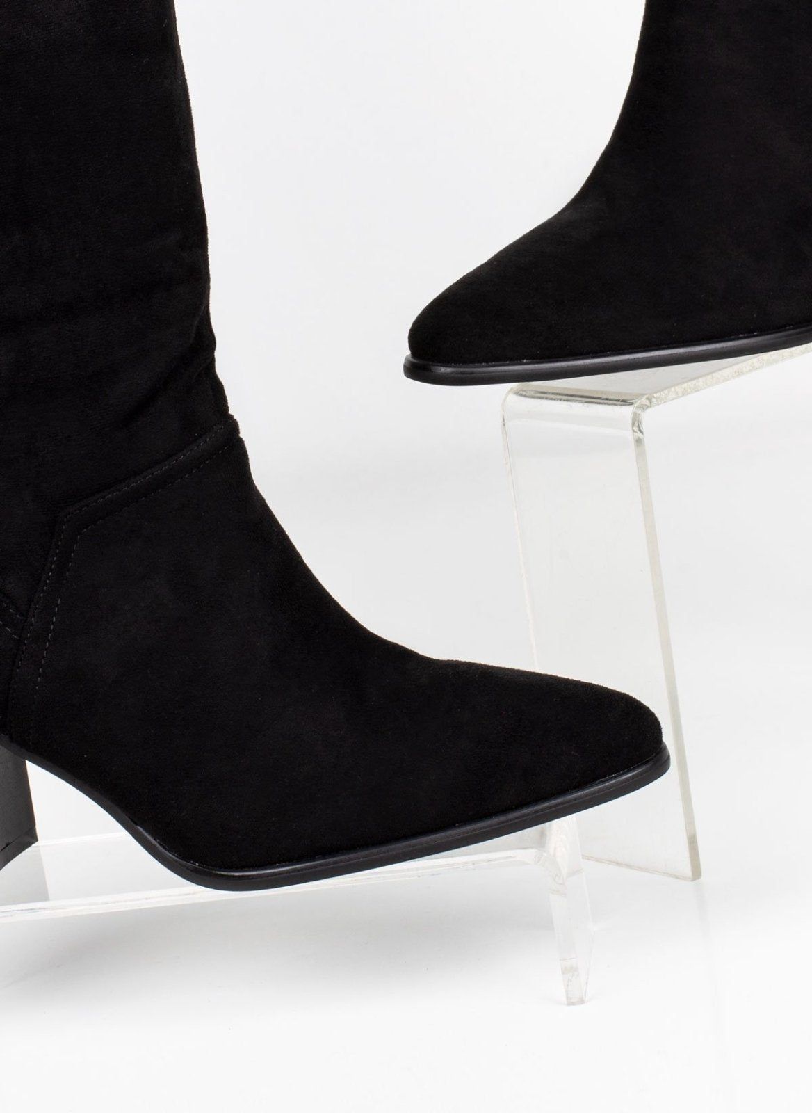 Close-up of black suede ankle boot toe and side seam, pointed toe on clear display stand