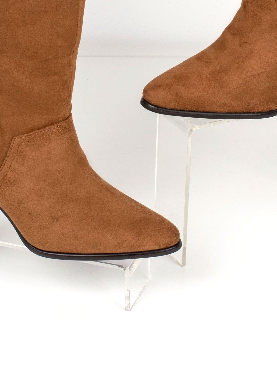 Close-up of tan suede ankle boot with pointed toe and stitched side seam, on clear display stand