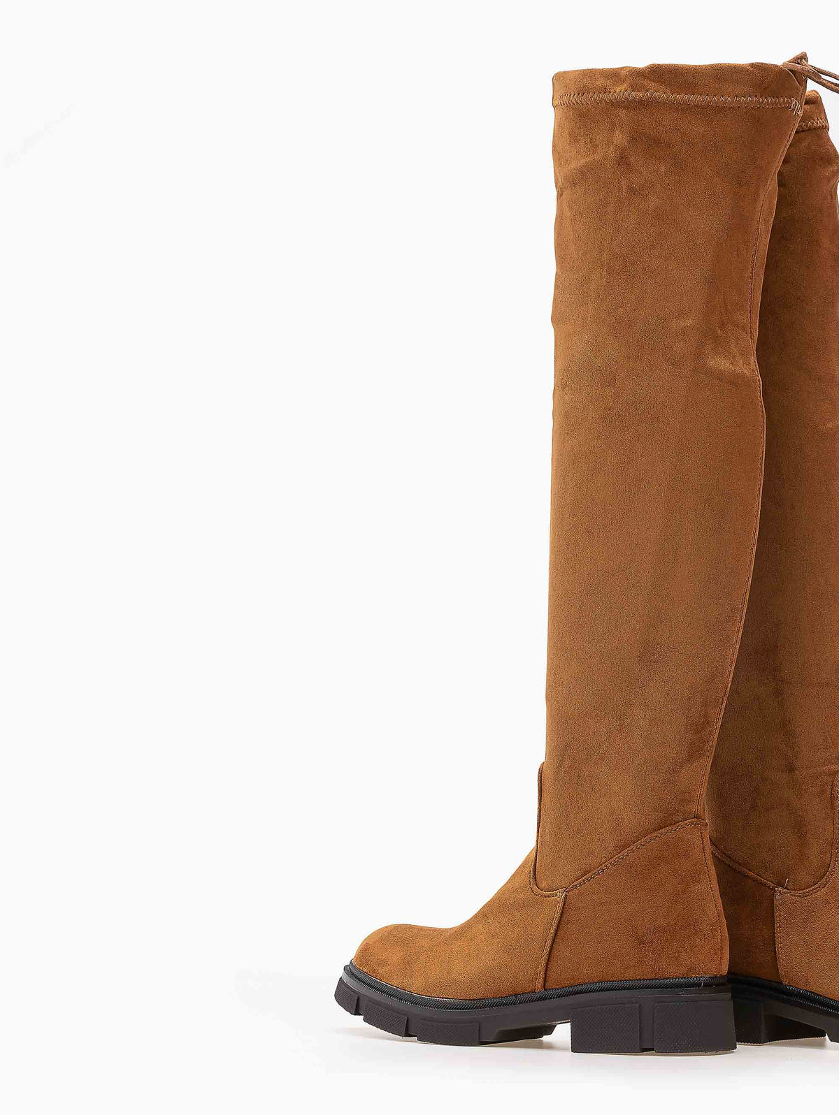 Tan faux suede over-the-knee boots with chunky black lug soles and stitched top edge, rear angled view on white