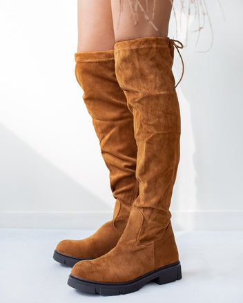 Tan faux suede over-the-knee boots with slouchy shaft and chunky black lug sole, worn on model, side view