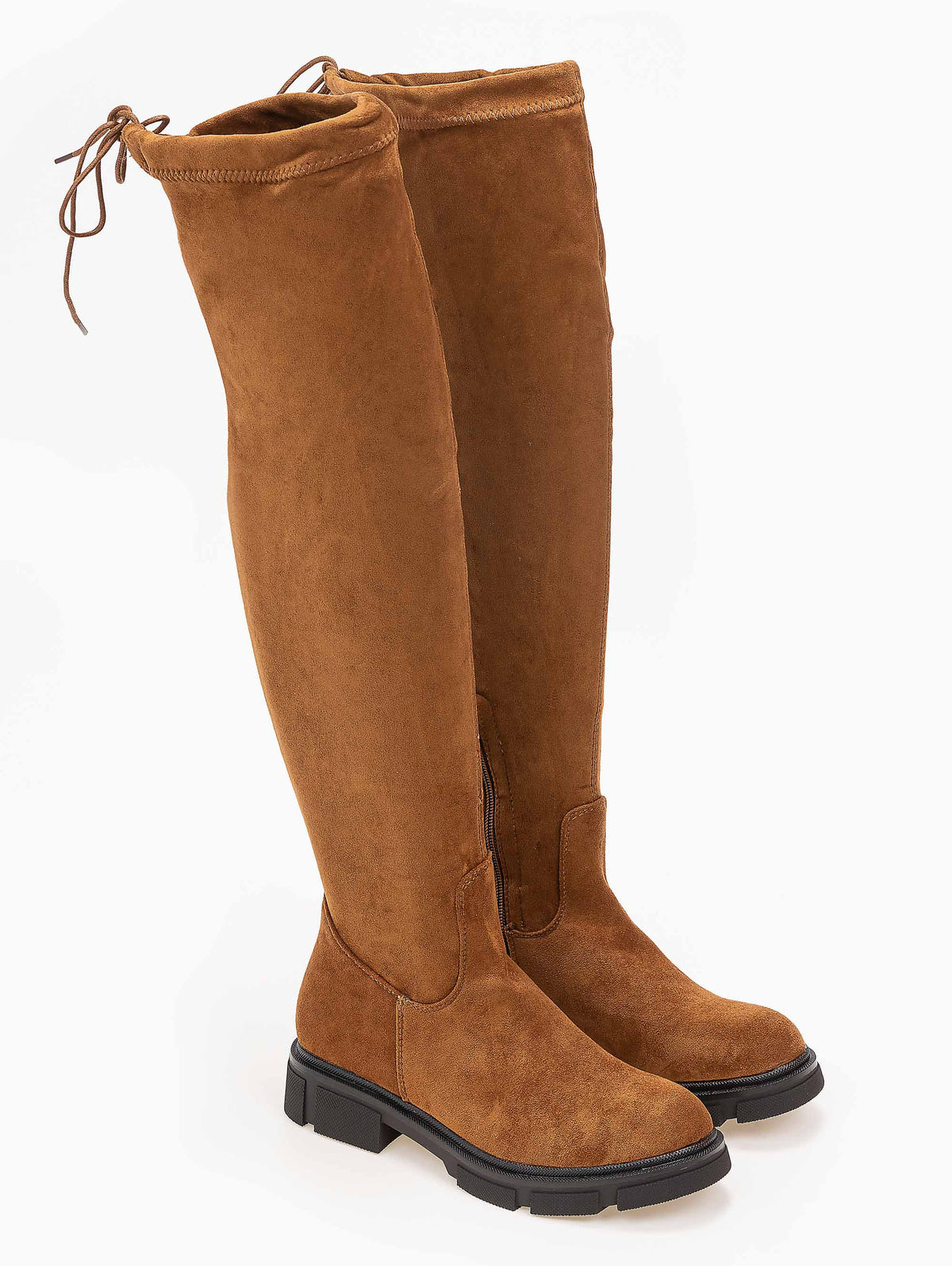 Pair of tan faux suede over-the-knee boots with back drawstring ties and chunky black lug soles, angled view on white