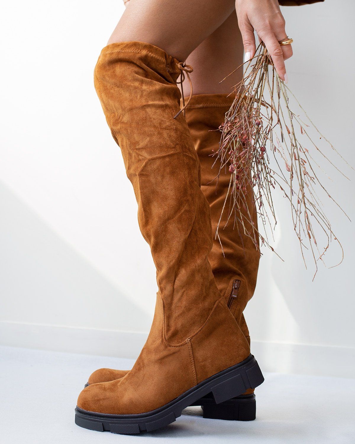 Tan faux suede over-the-knee boots with inner side zip, drawstring top and chunky black sole, worn on model, side view