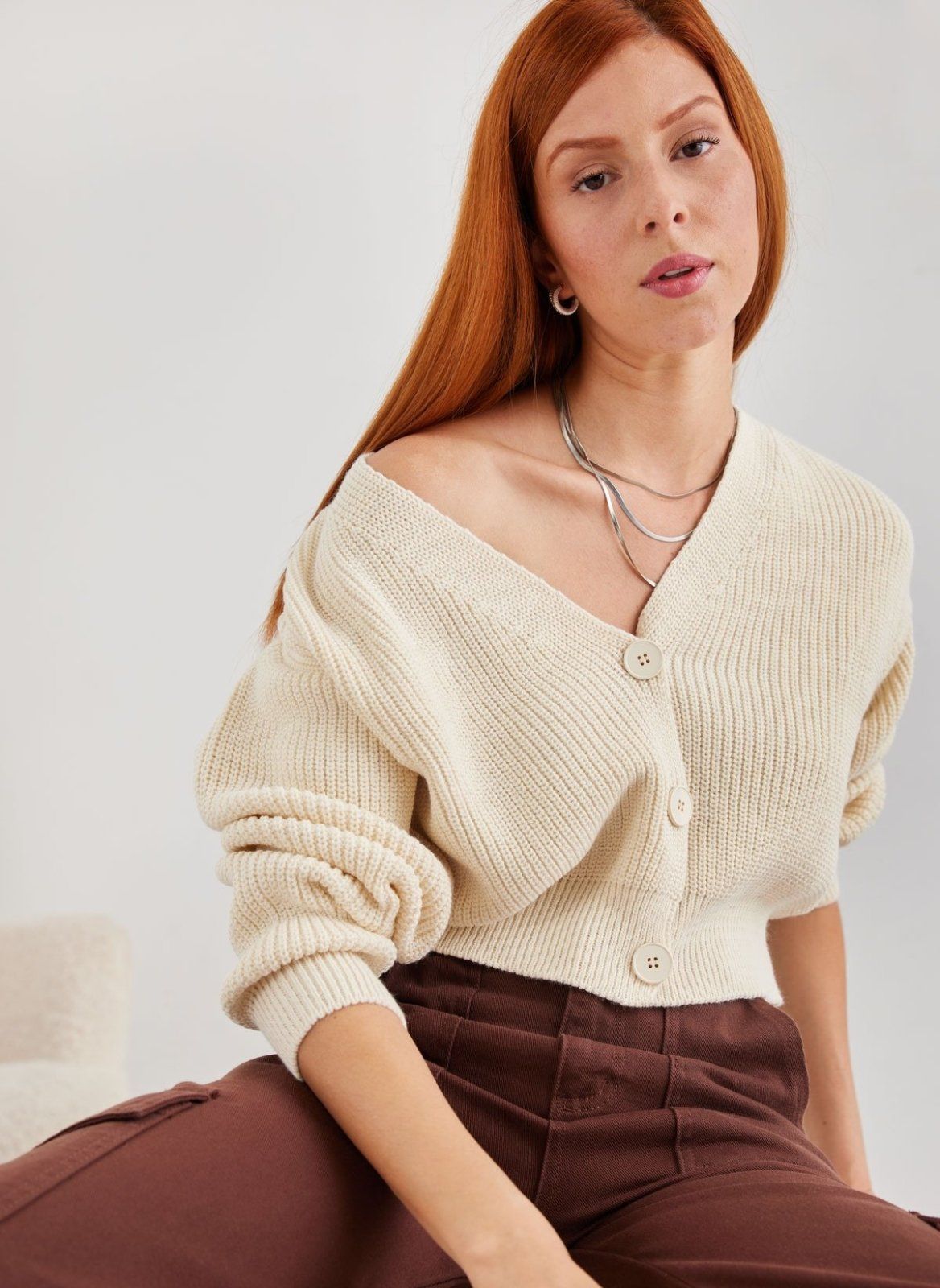 Cream chunky knit V neck button cardigan with knit detail, close-up of model seated, front view