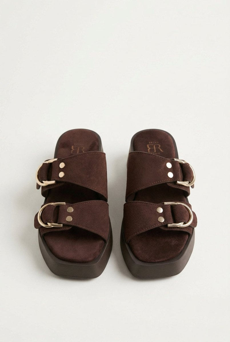 Pair of brown suede platform sandals with gold ring buckles and rivets, seen from the front showing square toes