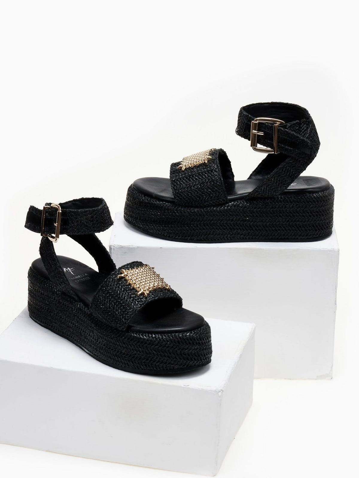 Pair of black woven raffia platform sandals with ankle buckle straps, displayed on white blocks
