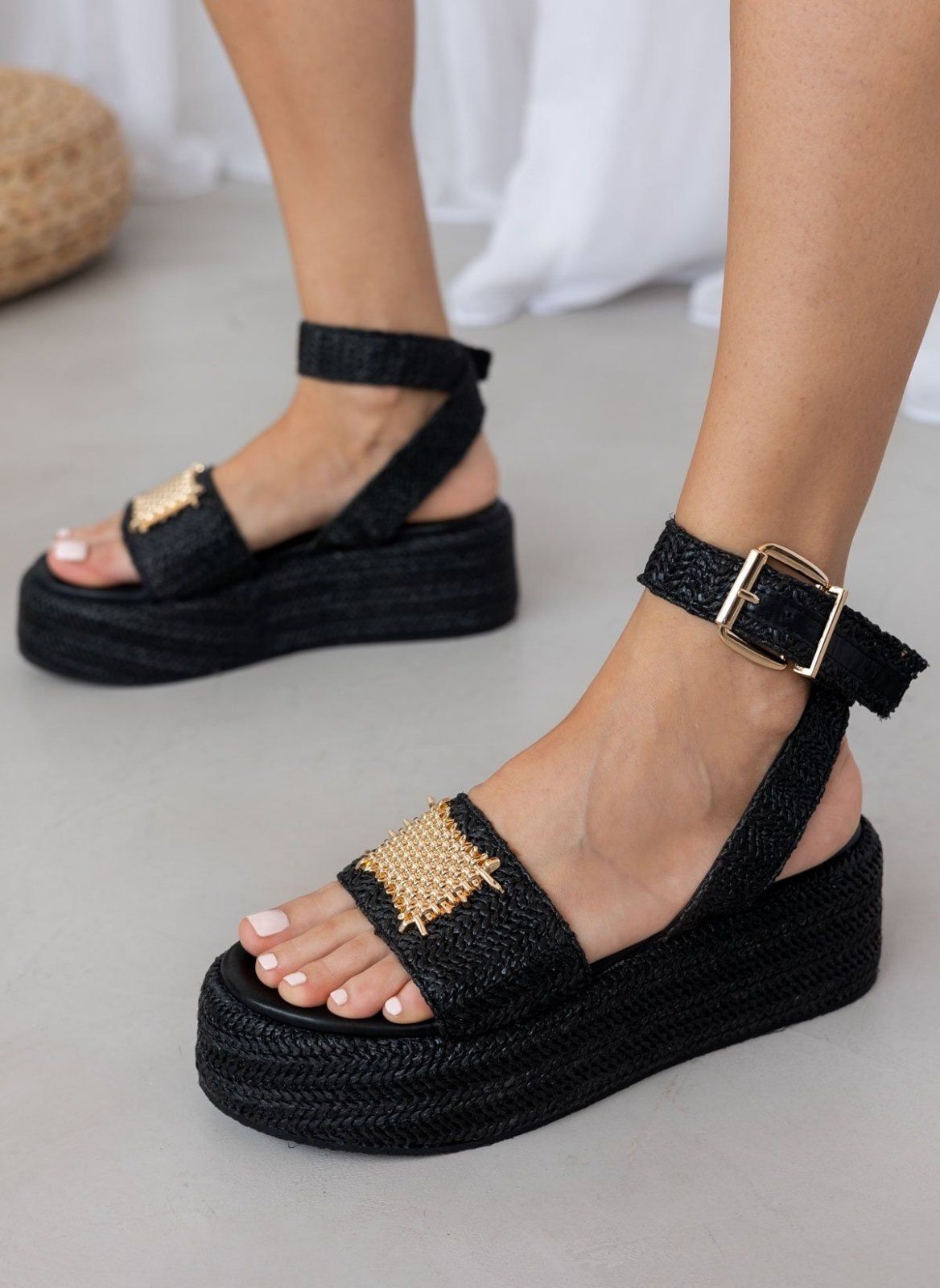 Model wearing black woven raffia platform sandals with buckled ankle strap and gold mesh patch, side view