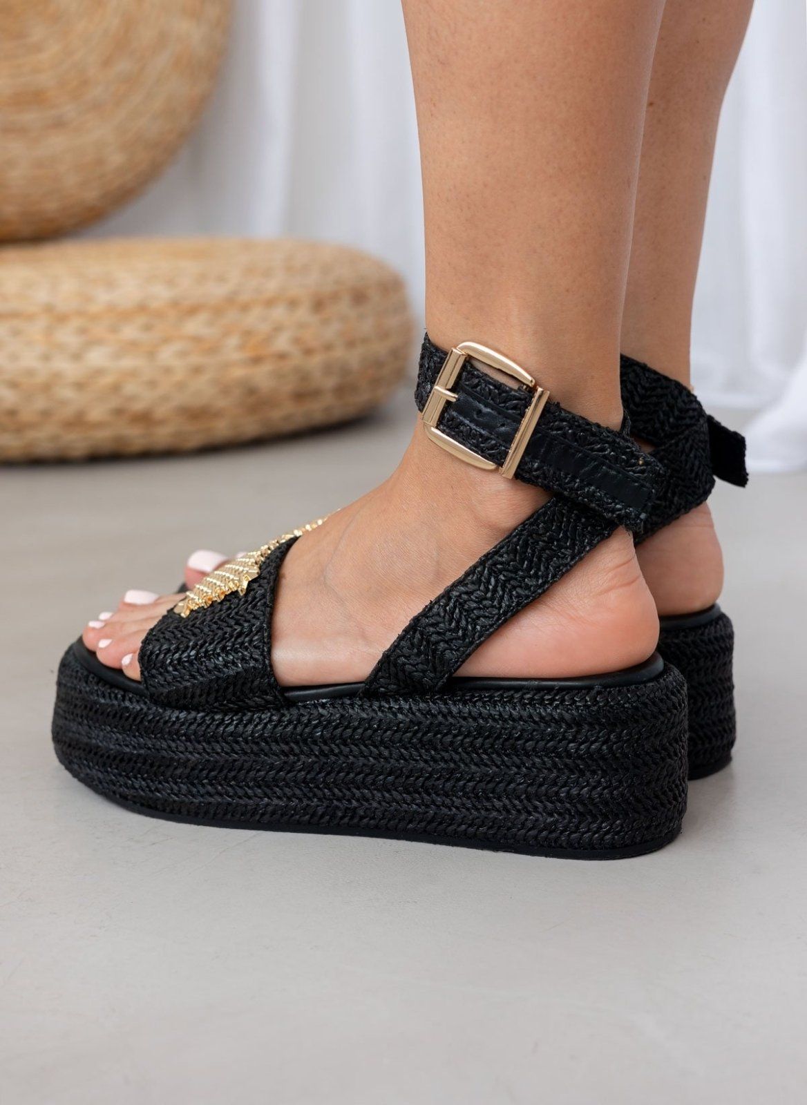 Model wearing black woven raffia platform sandals with buckled ankle strap, side view