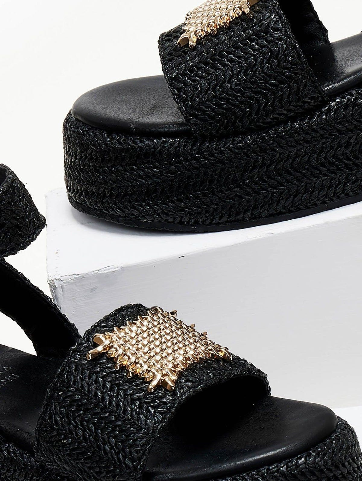 Close-up of black woven raffia platform sandal with gold mesh patch on the wide strap