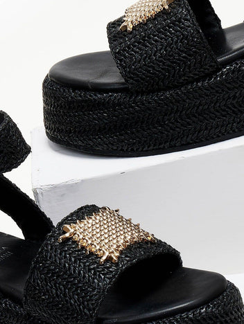 Close-up of black woven raffia platform sandal with gold mesh patch on the wide strap