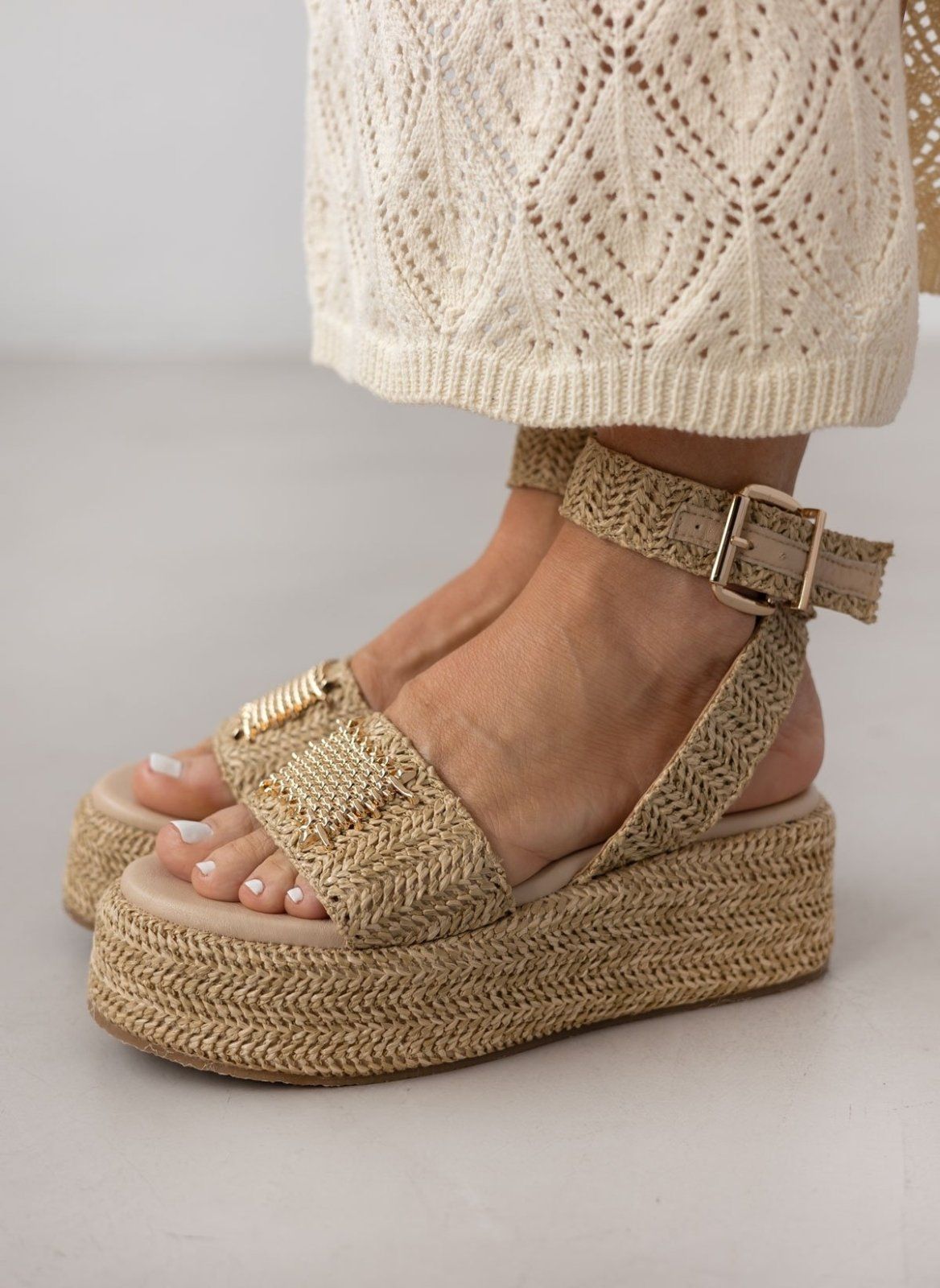 Model wearing natural raffia platform sandals with buckled ankle strap and white crochet trousers
