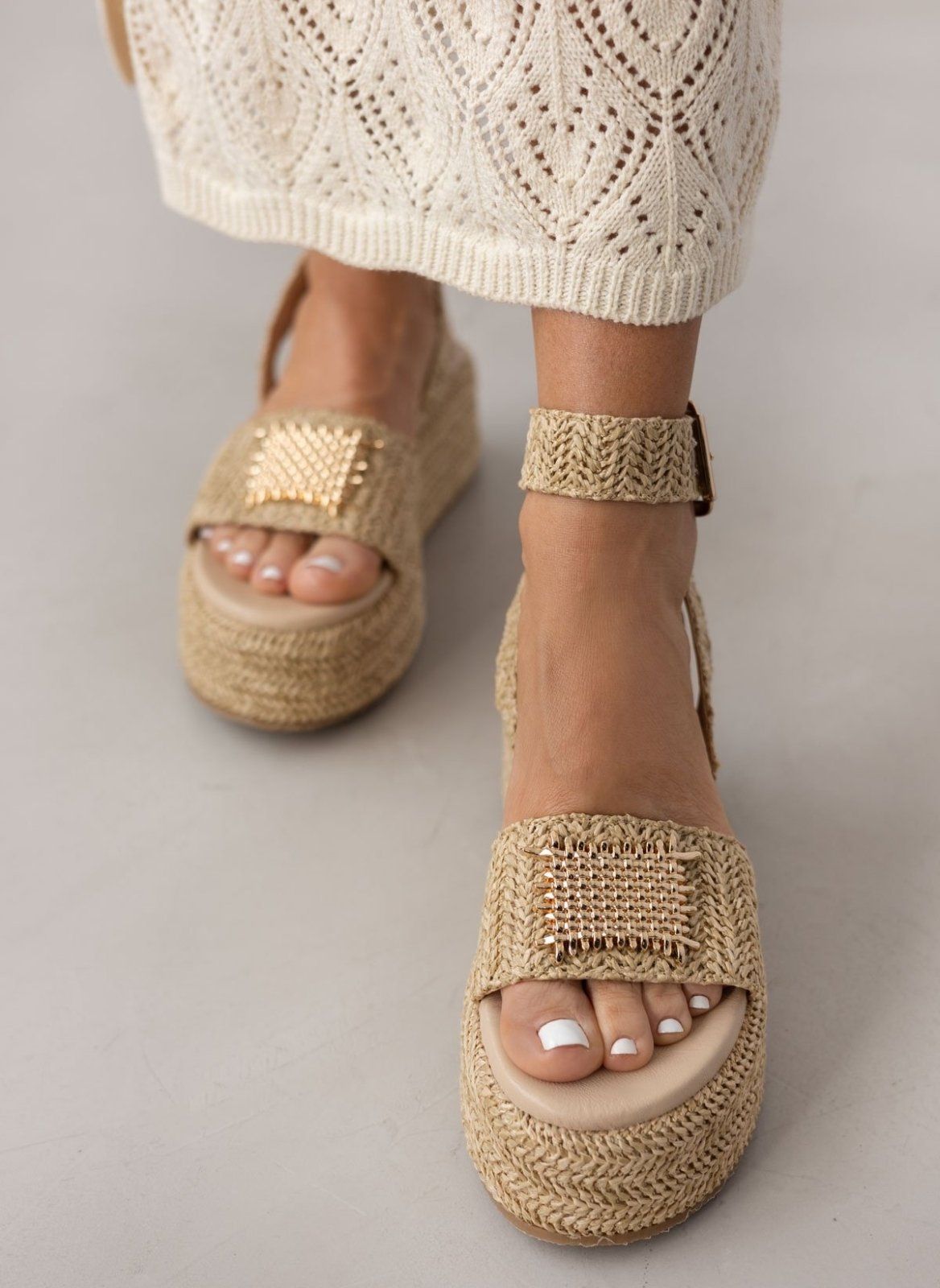 Model wearing natural raffia platform sandals with gold plate detail, front view with white crochet skirt
