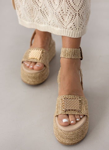 Model wearing natural raffia platform sandals with gold plate detail, front view with white crochet skirt