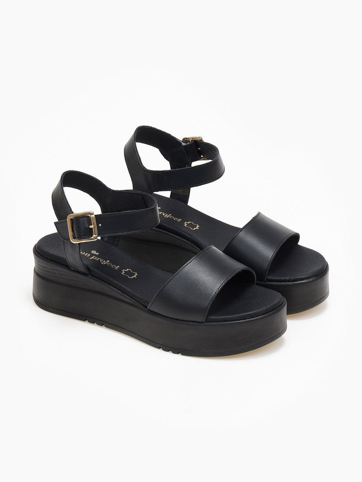 Pair of black leather flatform sandals with wide front strap and ankle buckle, three-quarter view