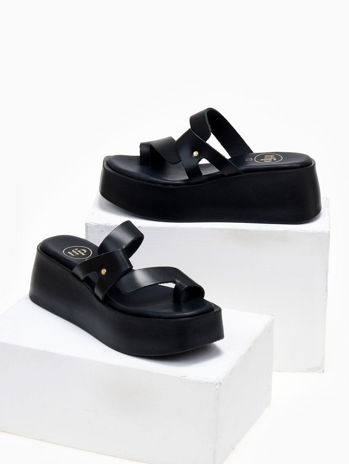 Pair of black leather platform slide sandals with crossover toe loop straps, displayed on white blocks