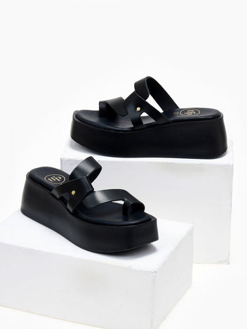 Pair of black leather platform slide sandals with crossover toe loop straps, displayed on white blocks