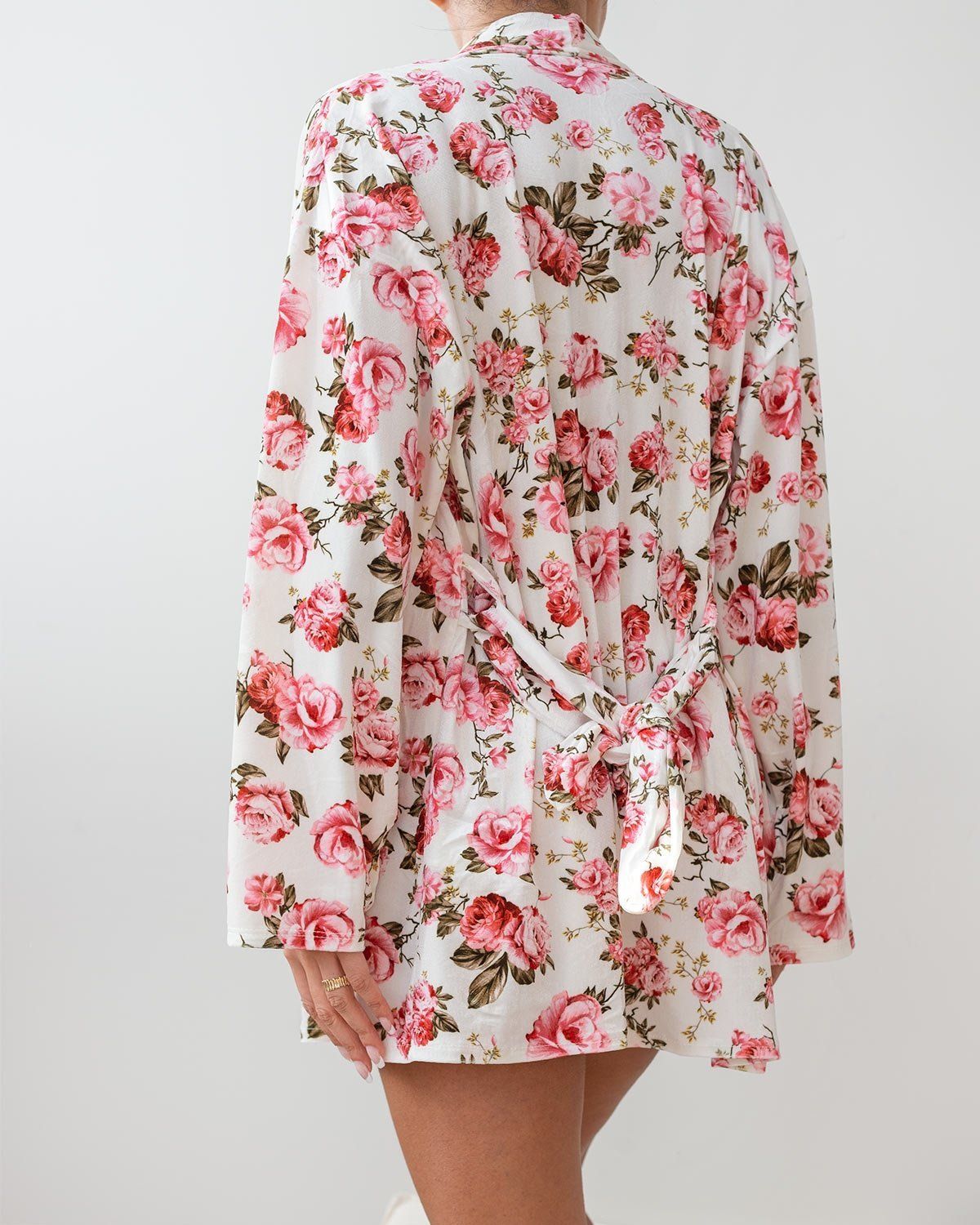 White velvet robe with pink and red rose floral print, wide sleeves and knotted tie belt at the waist, worn on model, back view