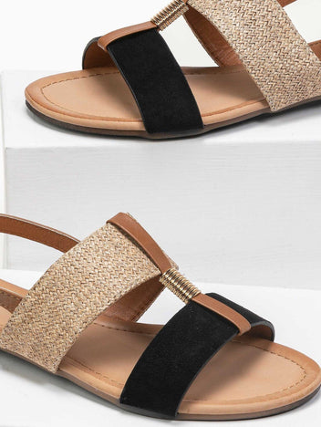 Close-up of black suede and woven straw flat sandals with tan leather trim, gold coil detail and tan insole, shown on white blocks