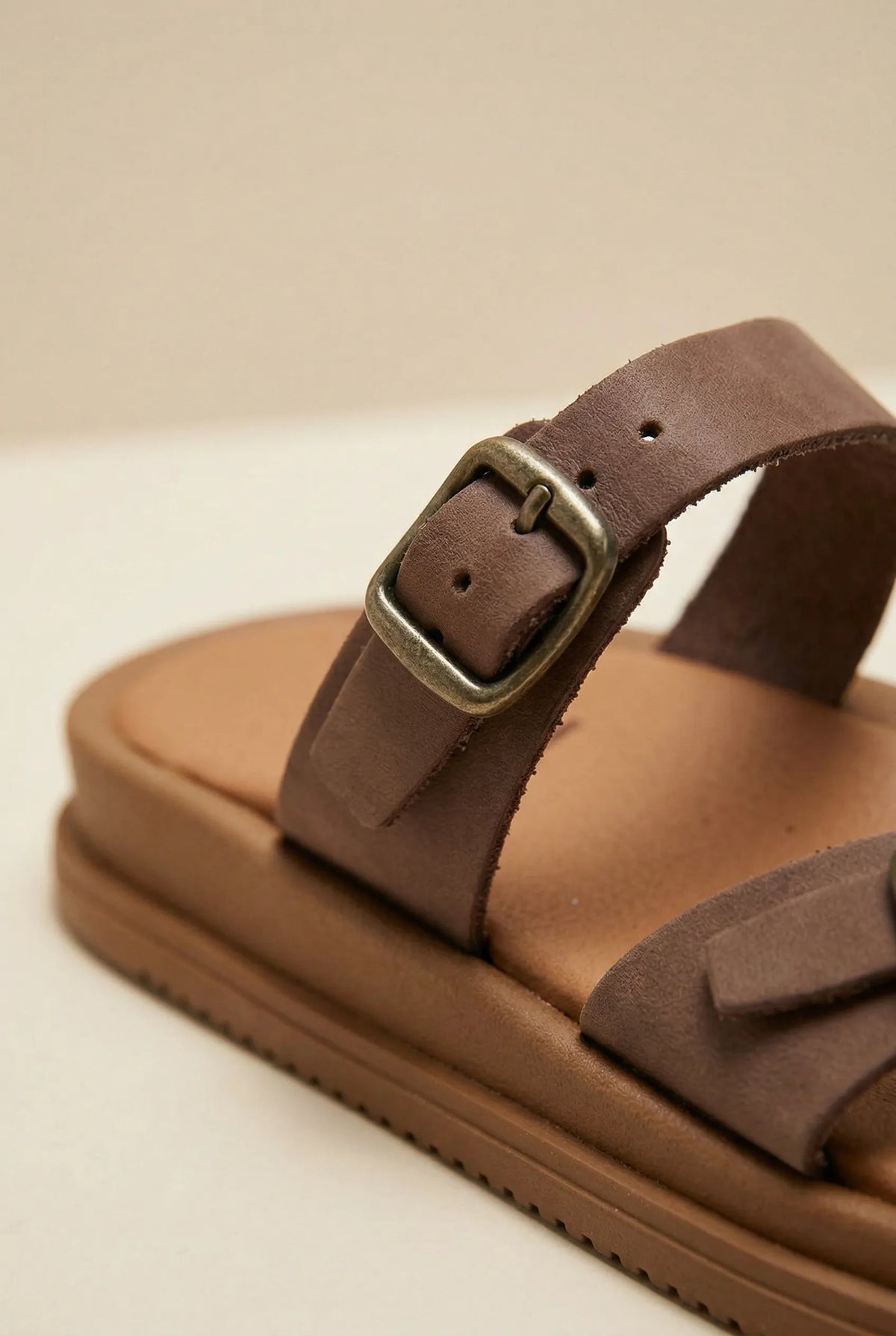 Close-up of a brown leather buckled strap on a slide sandal with thick tan sole and padded footbed