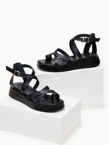 Pair of black leather crossover strap platform sandals with toe loop and ankle buckle, on white blocks