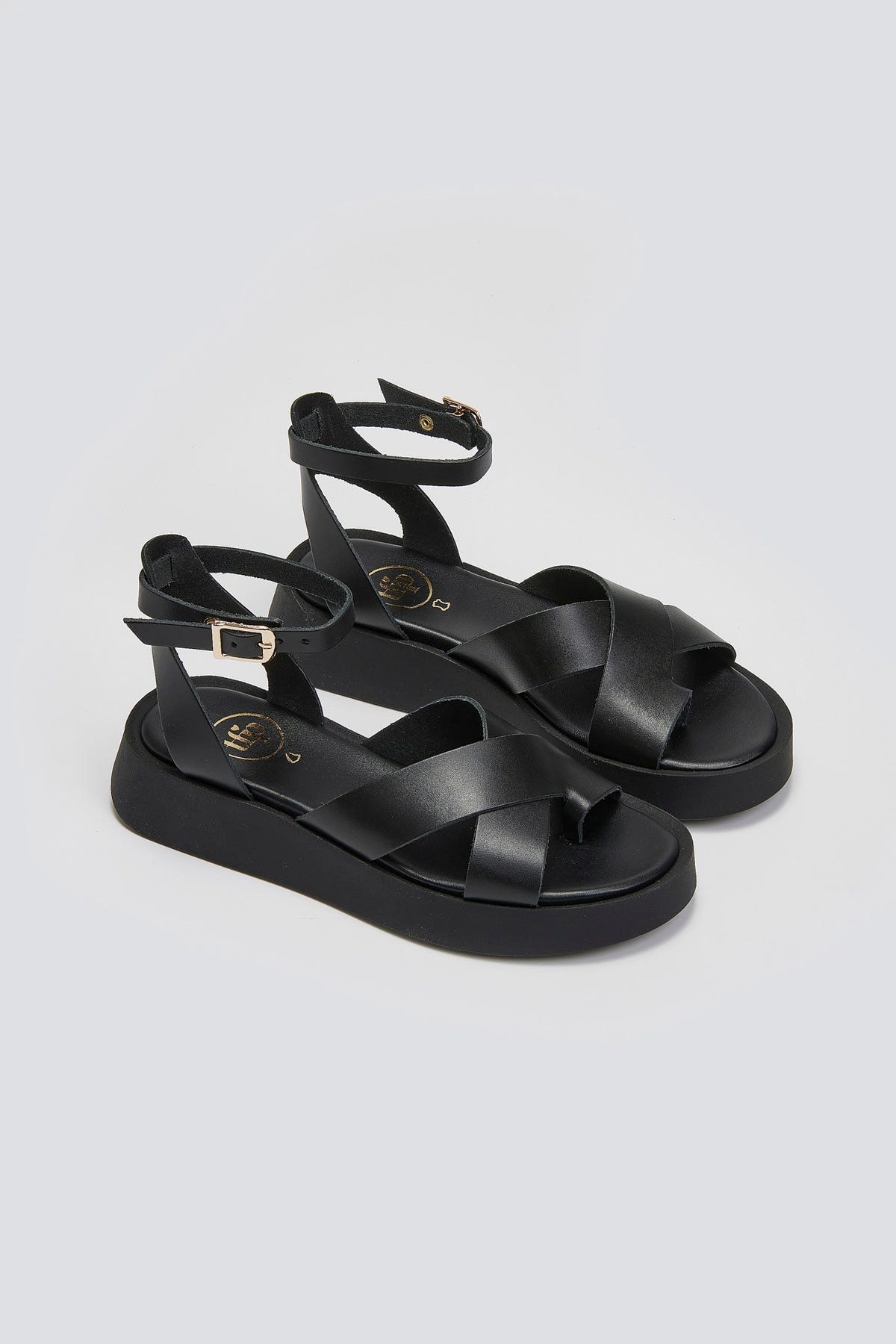 Pair of black leather crossover strap platform sandals with ankle buckle, three-quarter view