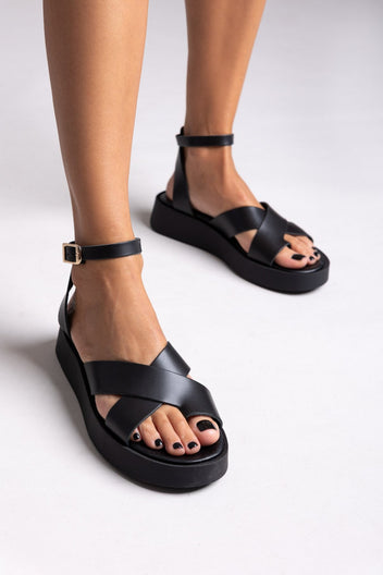 Model wearing black leather crossover strap platform sandals with ankle strap, front view of feet