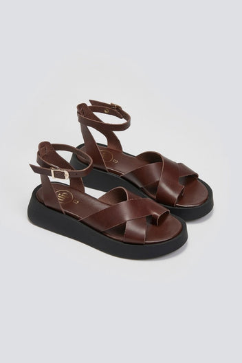 Pair of brown leather crossover strap platform sandals with ankle buckle and black sole, three-quarter view
