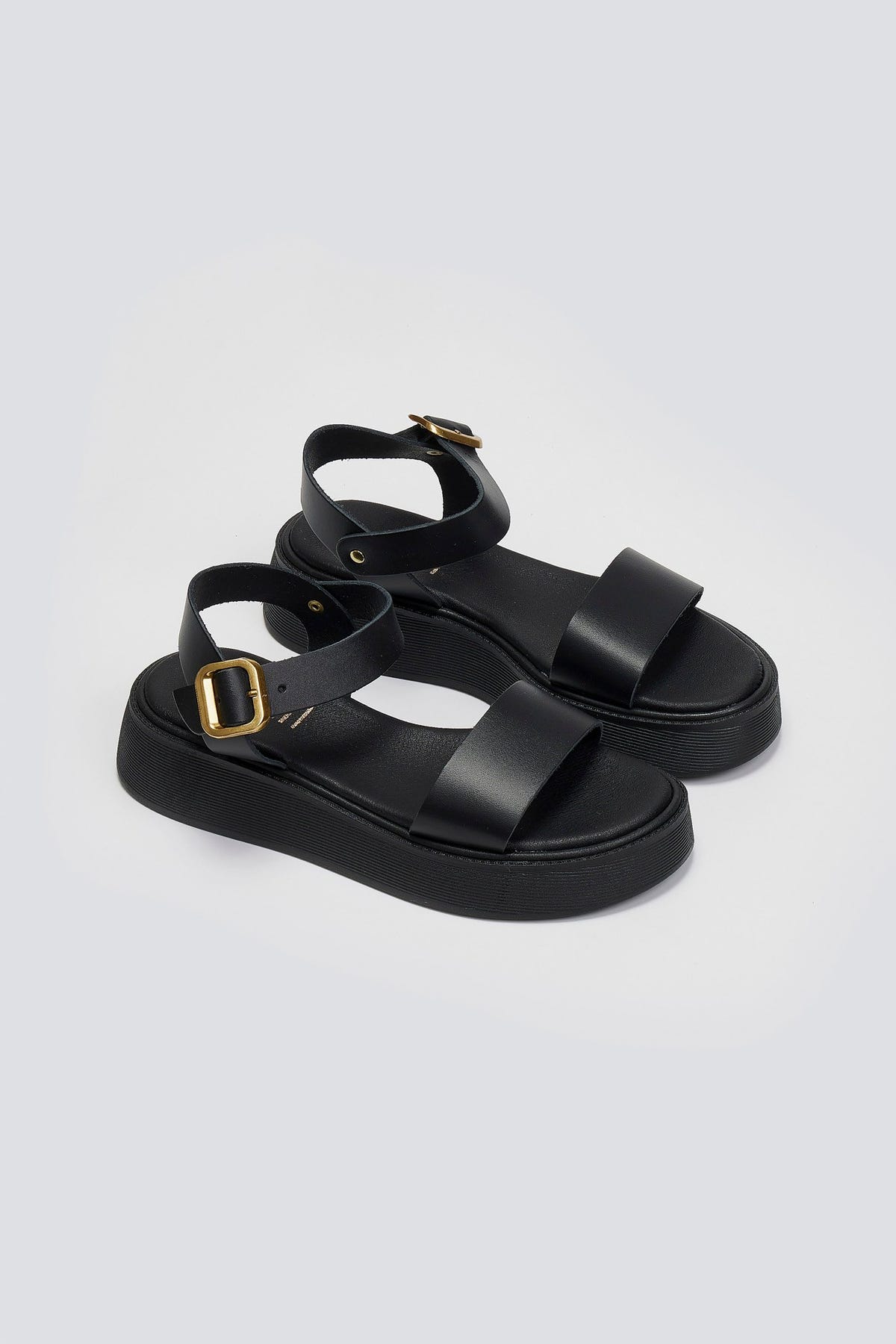 Pair of black leather platform sandals with wide front strap and gold ankle buckle, three-quarter view