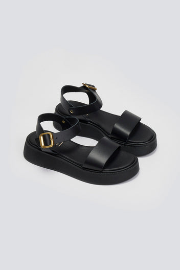 Pair of black leather platform sandals with wide front strap and gold ankle buckle, three-quarter view