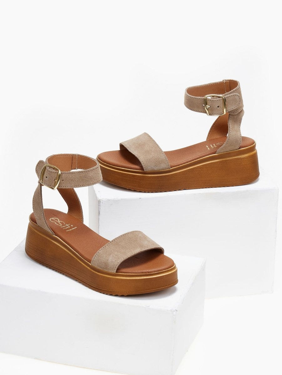 Pair of taupe suede wedge platform sandals with ankle strap and tan sole, on white blocks
