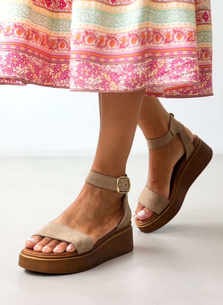 Model wearing taupe suede wedge platform sandals with ankle buckle strap and pink floral skirt