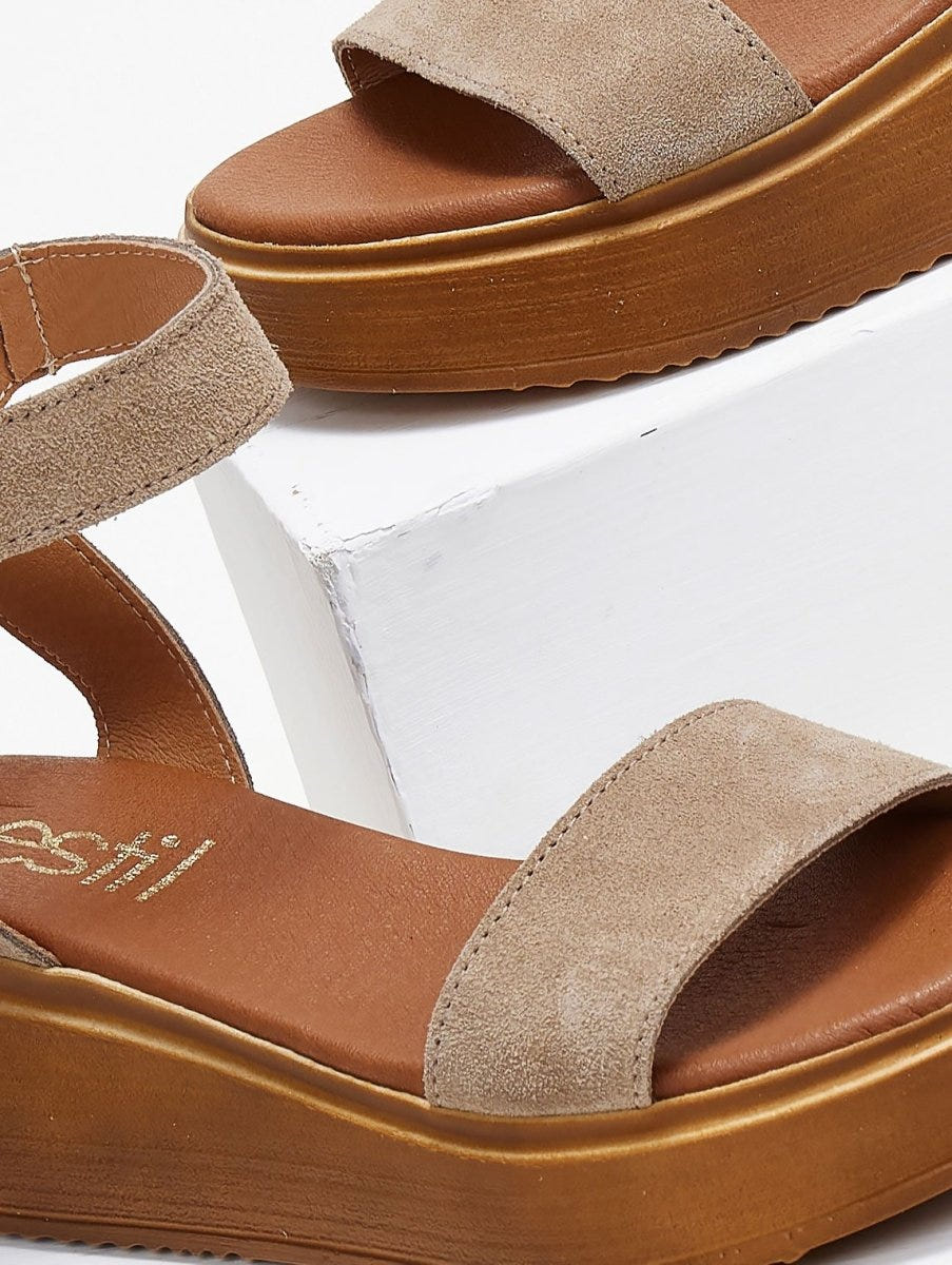 Close-up of taupe suede wedge platform sandal with wide strap and tan sole on a white block