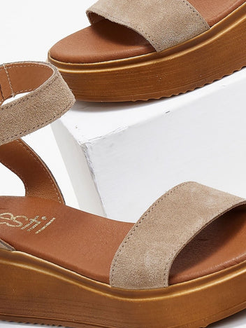 Close-up of taupe suede wedge platform sandal with wide strap and tan sole on a white block