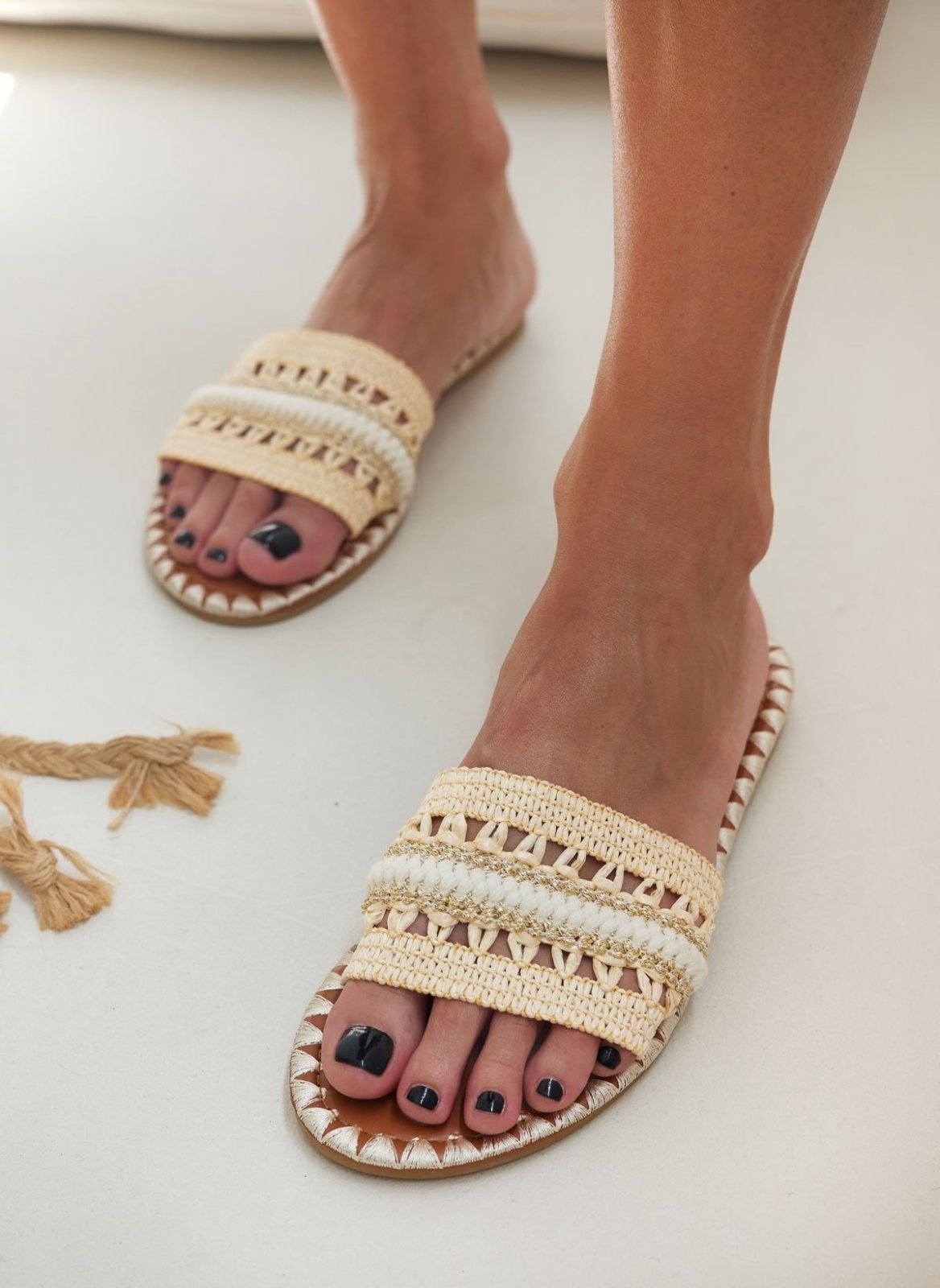Model wearing natural raffia slide sandals with woven cream and white band, high angle view