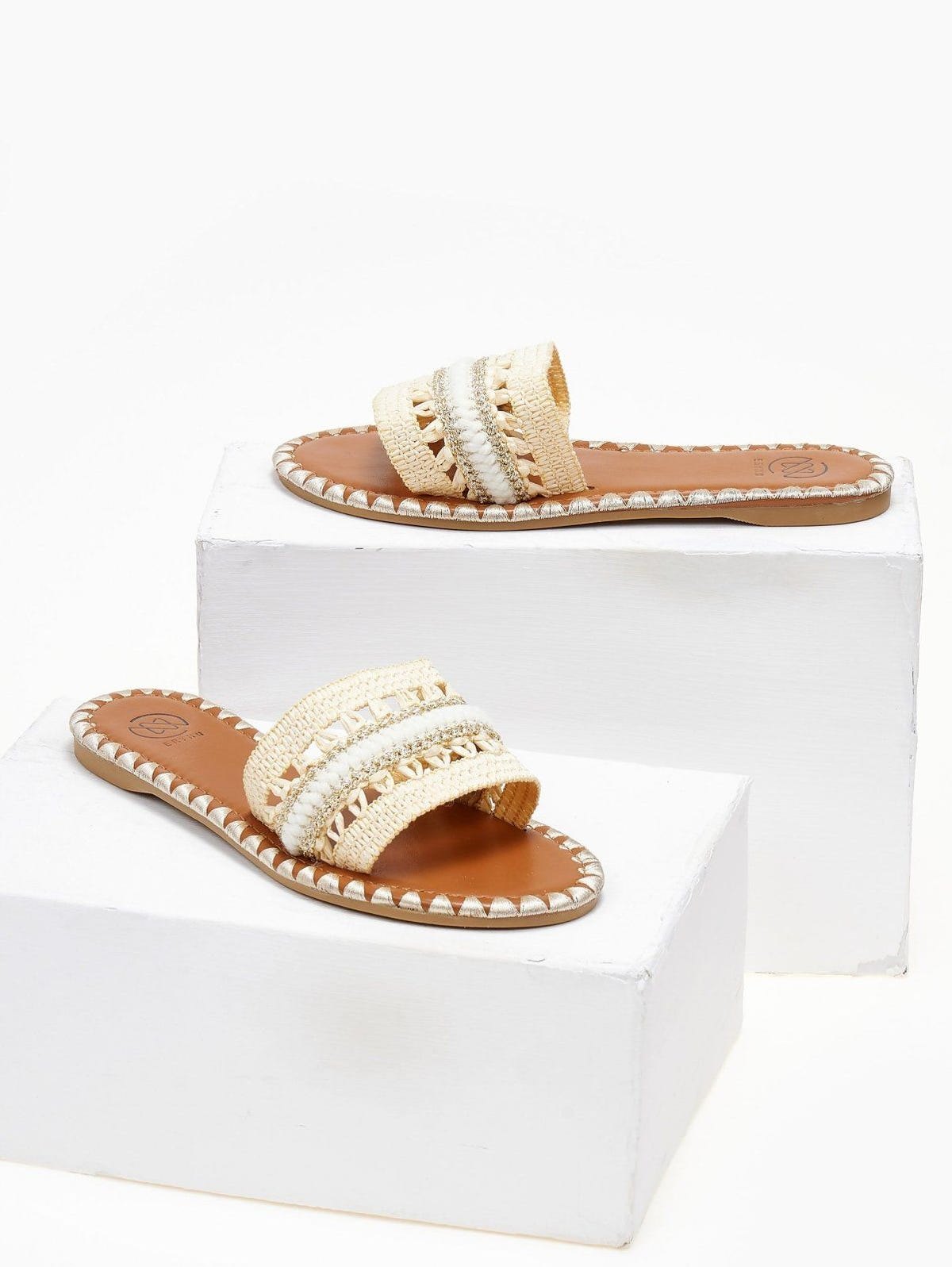 Pair of natural raffia slide sandals with woven cream and white band, displayed on white blocks