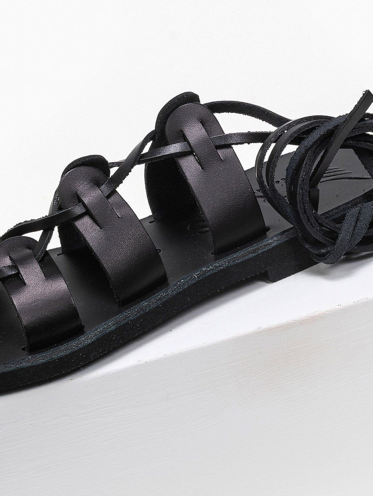 Close-up of black leather lace-up flat sandal with toe loop and wrapped ankle ties