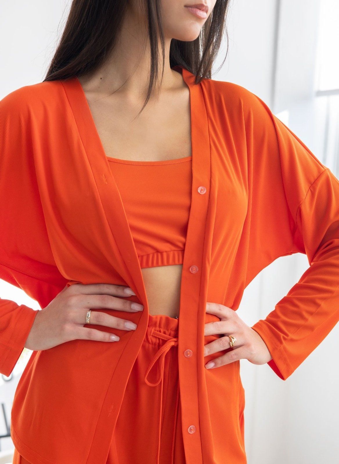 Close-up of orange ribbed pyjama button-front shirt over camisole top and drawstring trousers, worn on model