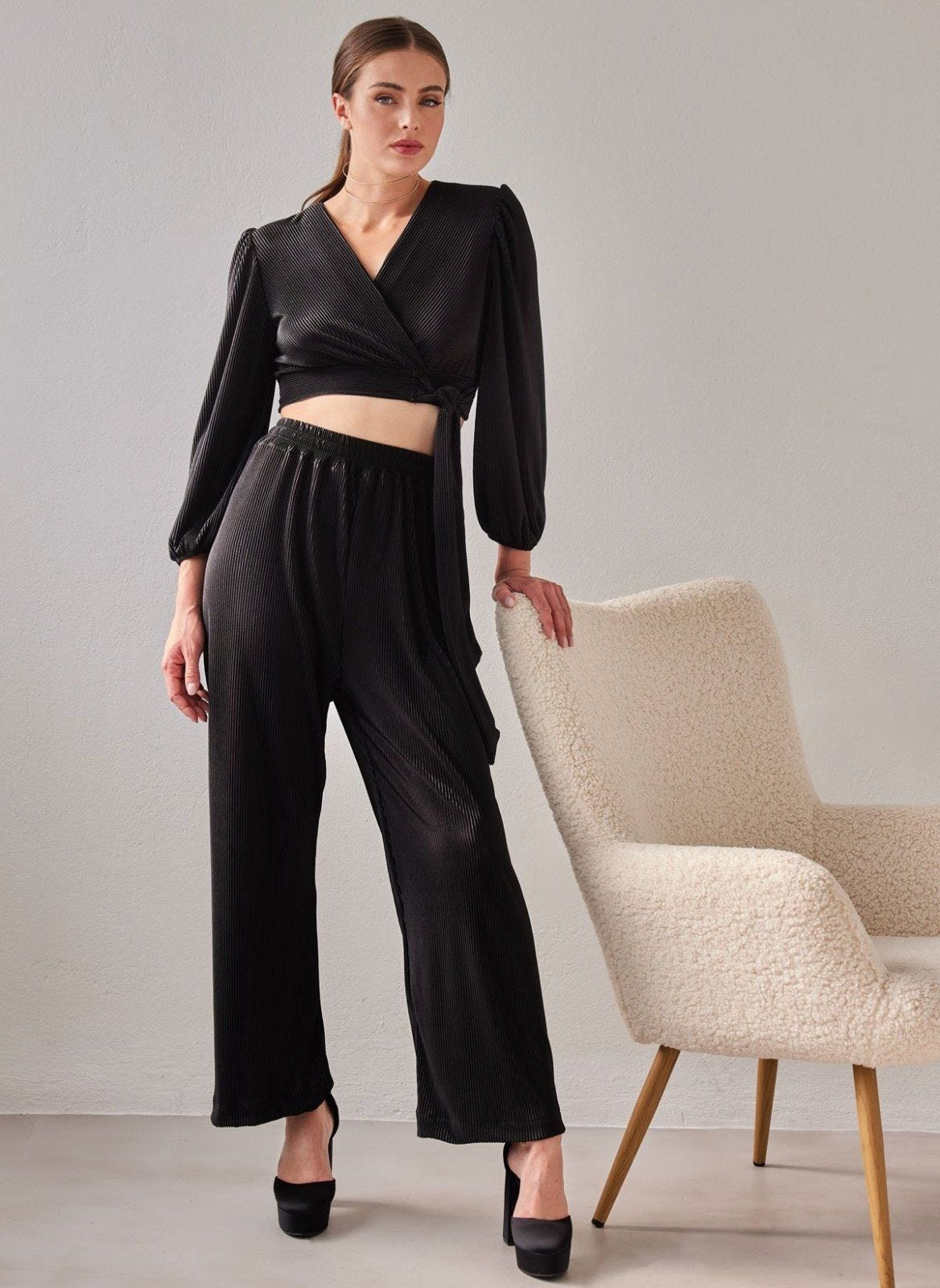 Black ribbed pleated satin wrap crop top with V-neck, balloon sleeves and side tie, with matching wide leg elastic waist trousers, worn on model
