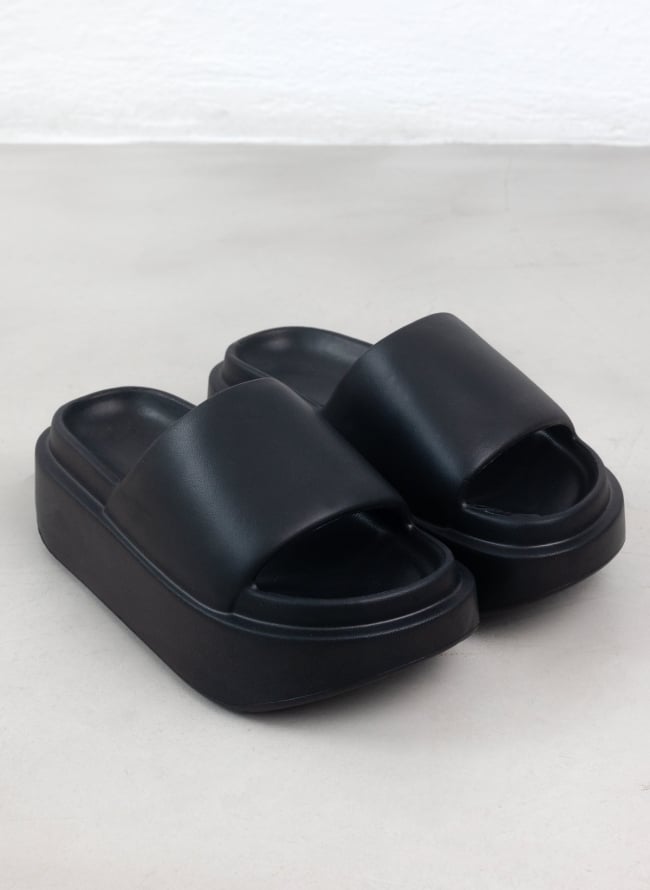 Pair of black matte platform slide sandals with wide padded strap and chunky sole, high angle view