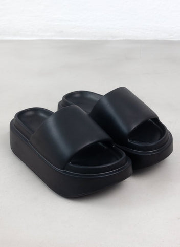 Pair of black matte platform slide sandals with wide padded strap and chunky sole, high angle view