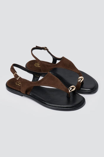 Pair of brown suede thong sandals with black soles, angled to show the round metal ornament and ankle strap buckle