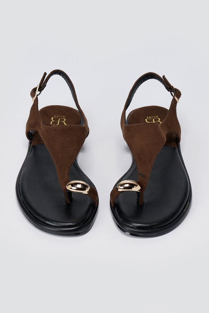 Pair of brown suede thong sandals with black soles and a round gold tone ornament, top view with ankle straps open