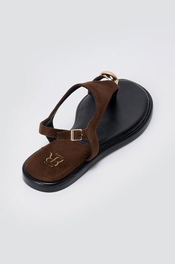 Single brown suede sandal seen from above at an angle, with a black leather sole and a buckled ankle strap