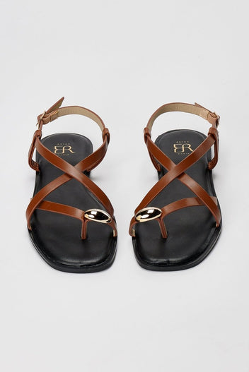 Pair of tan leather toe ring sandals seen from the front, crossed straps over the toes and gold ring above black footbed