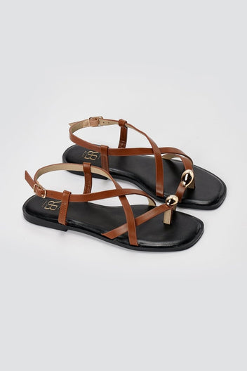 Pair of tan leather toe ring sandals on light grey, three-quarter view of crossed straps, gold ring at toe and black footbed