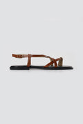 Tan leather toe ring sandal in side view showing thin straps, ankle buckle and a flat sole on light grey